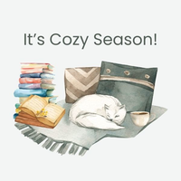 A cat curled up asleep on top of a blanket next to pillows. A mug of coffee is to the right of the cat, and a stack of books with another book open is to the left of the cat.